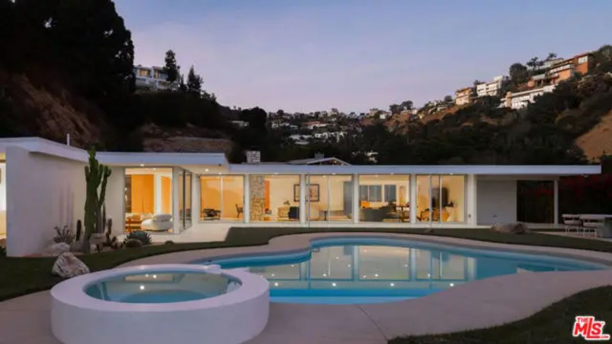 Elegant mid-century modern home with floor-to-ceiling glass windows, overlooking the illuminated pool. 