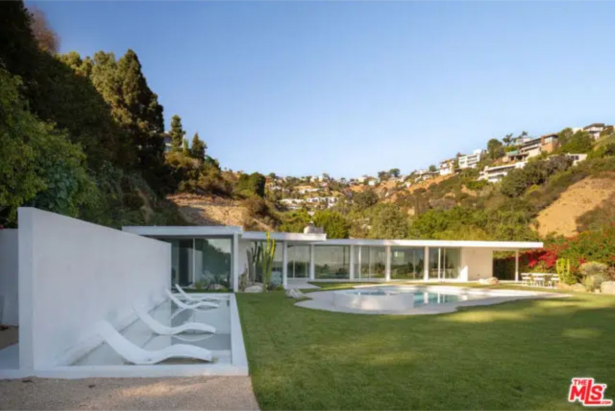Stunning modern home nestled in the hills, featuring a sleek glass design and a lush backyard with a pool.