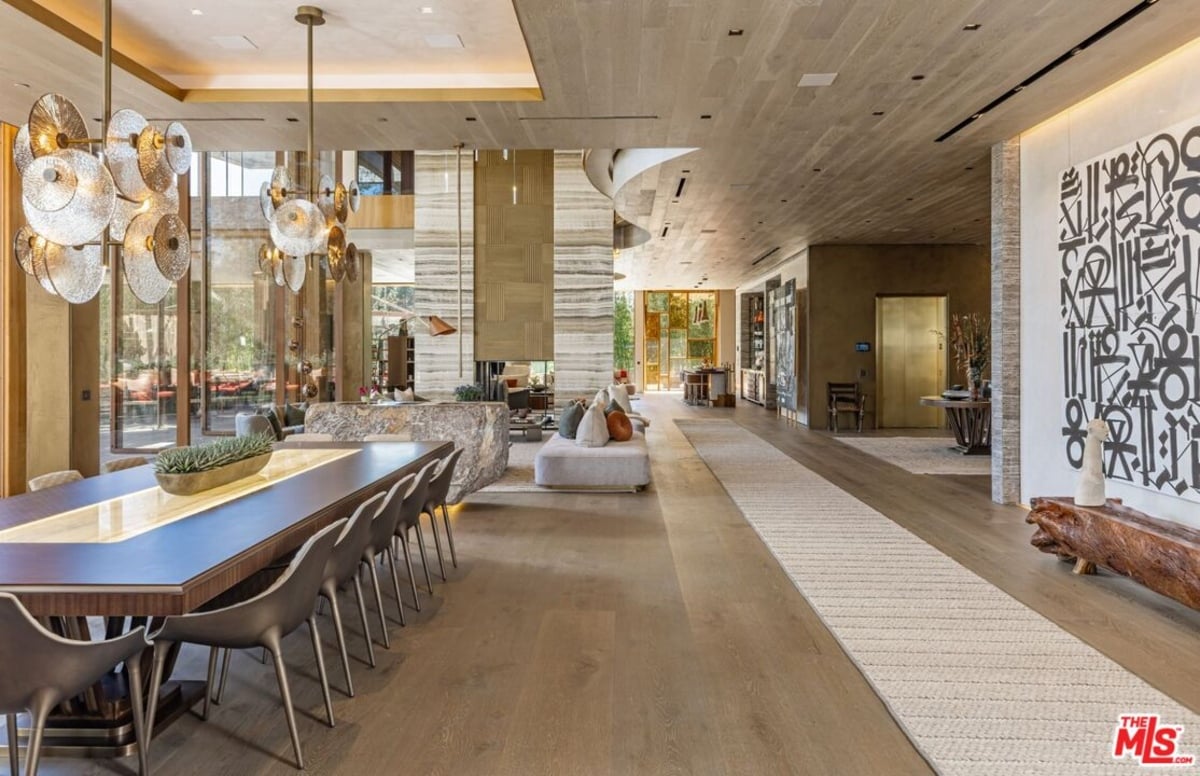 Dining and living area with sculptural lighting, long table, and seating arranged around stone fireplace. 