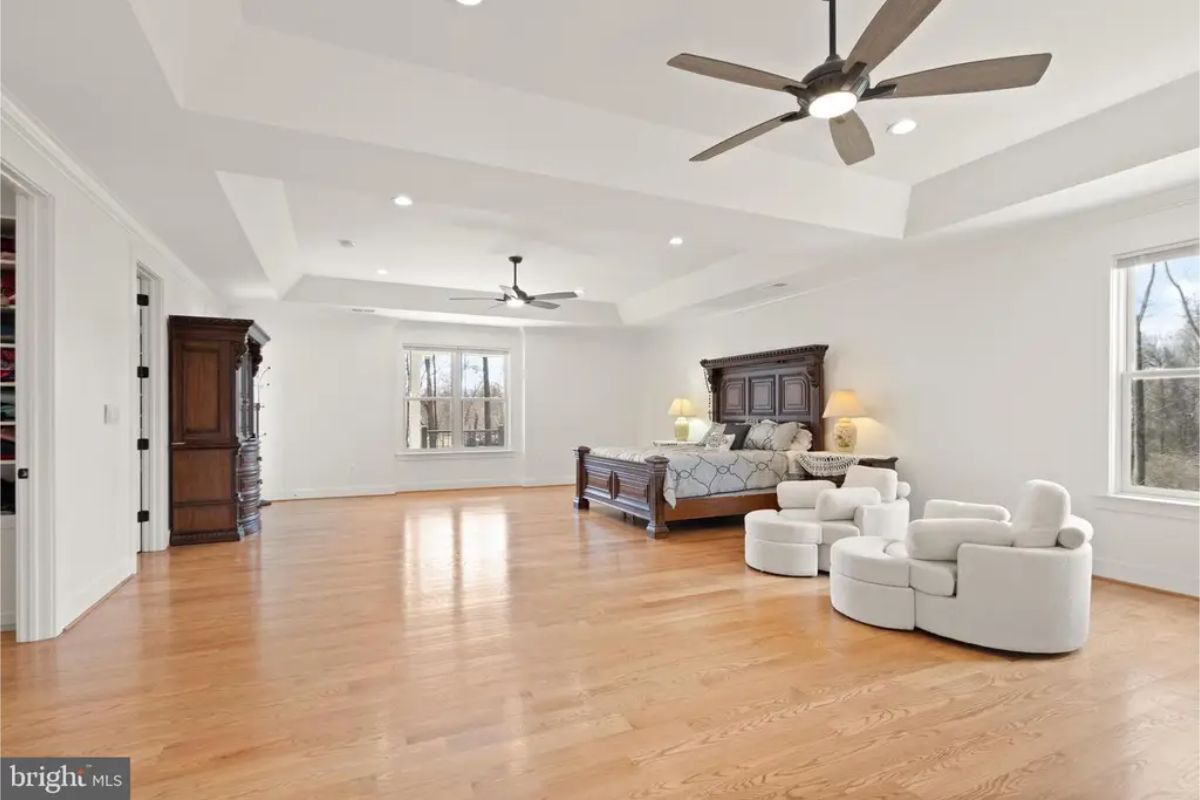 Spacious bedroom with tray ceiling, hardwood flooring, and multiple windows. 
