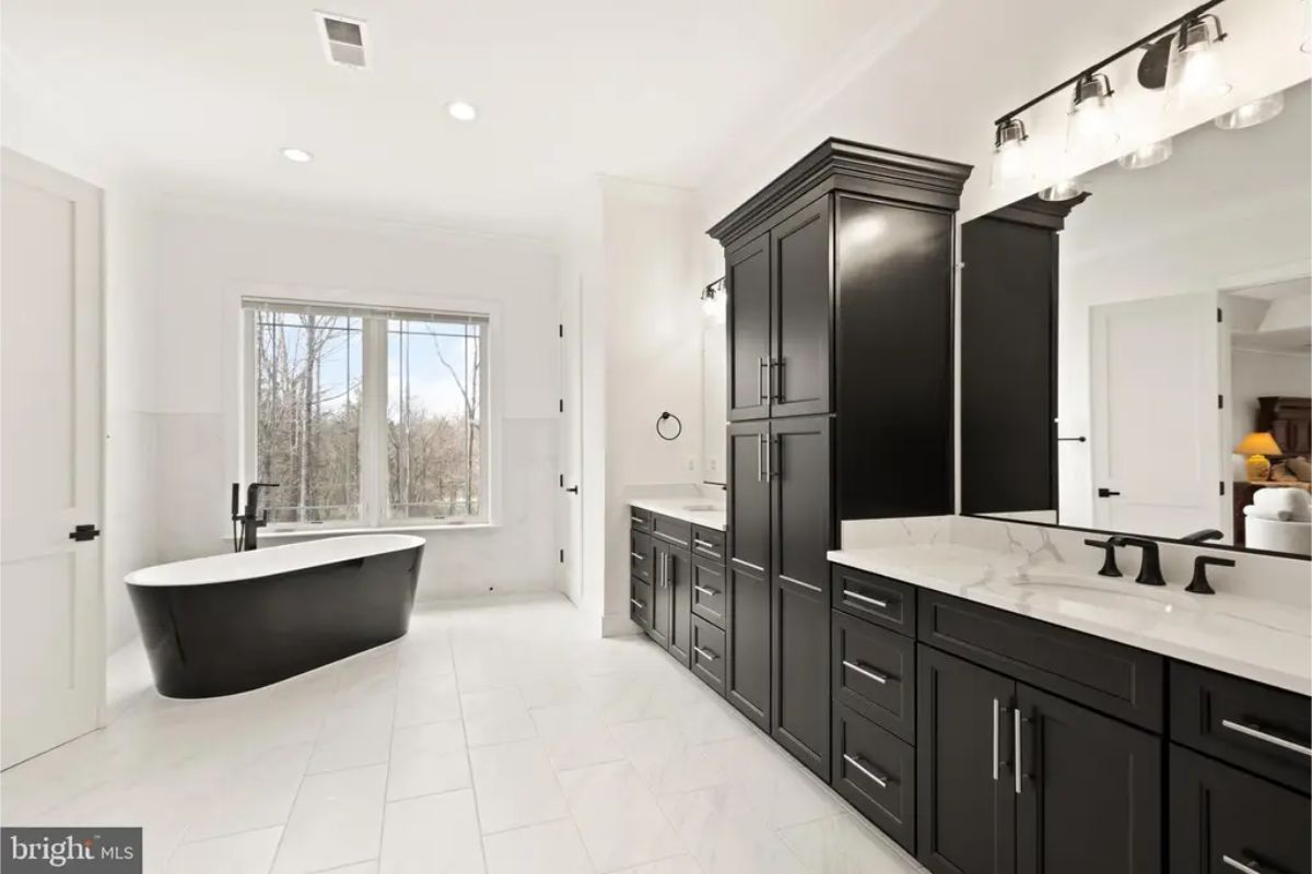 Bathroom with black cabinetry, freestanding tub, and white tile flooring. 