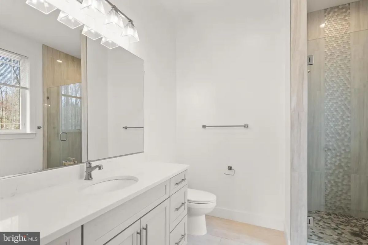 Bathroom with single-sink vanity, wall-mounted mirror, and glass-enclosed shower with accent tile. 