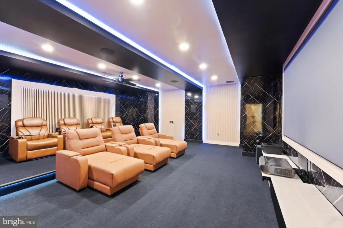 Home theater room with recliner seating, blue carpet, and large projector screen. 