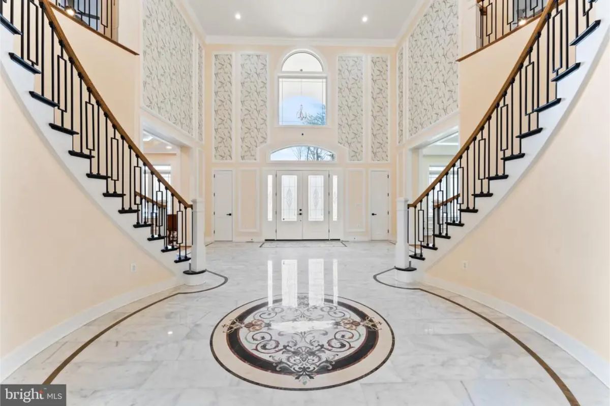 Double staircase foyer with patterned marble flooring and high ceiling. 