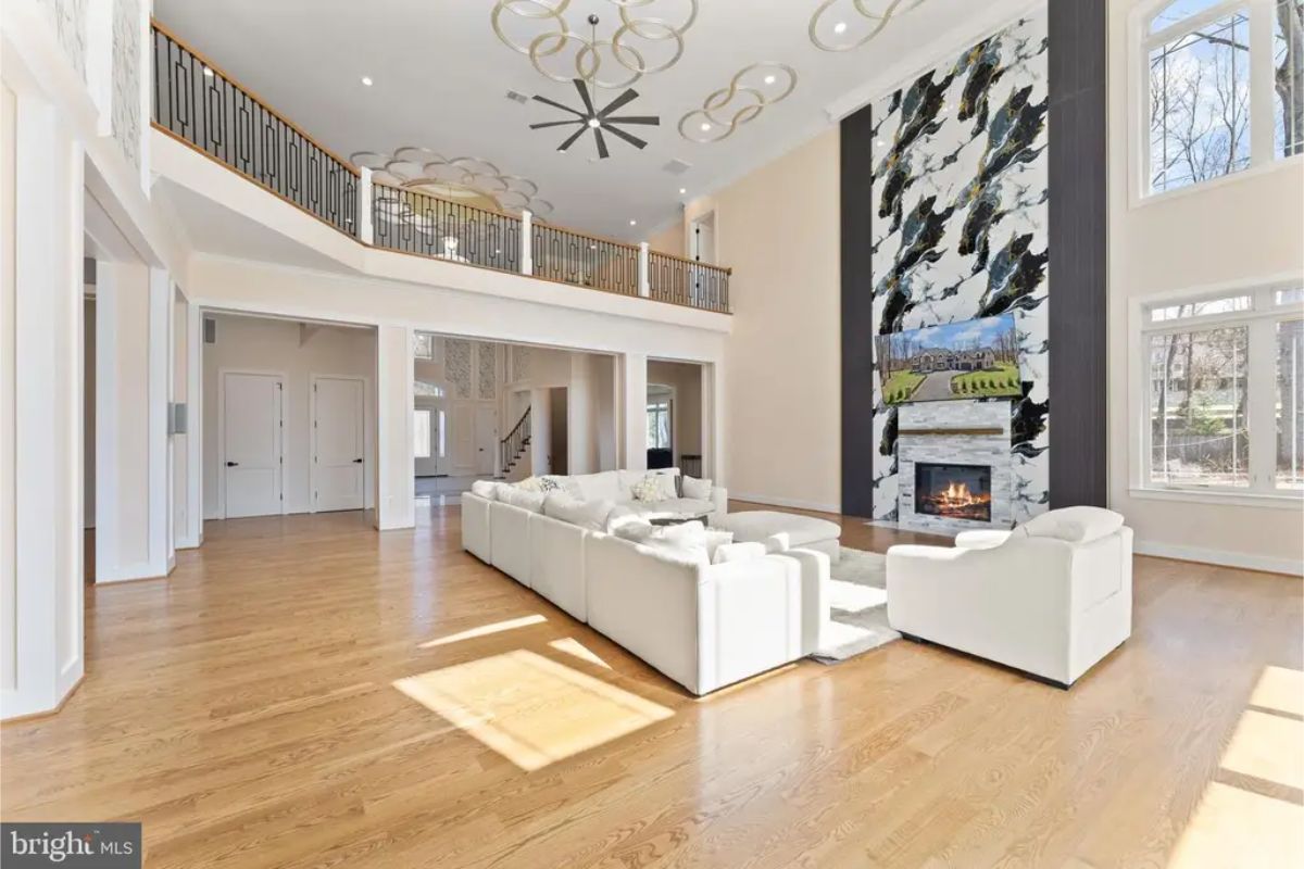 Living room with tall fireplace, white sectional, and open second-floor balcony. 