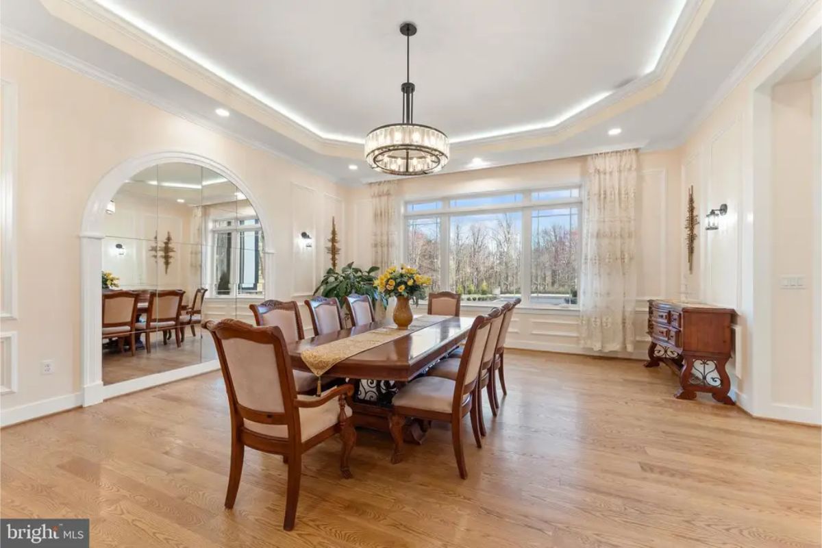 Dining room with wood table, ten chairs, and tray ceiling with chandelier. 