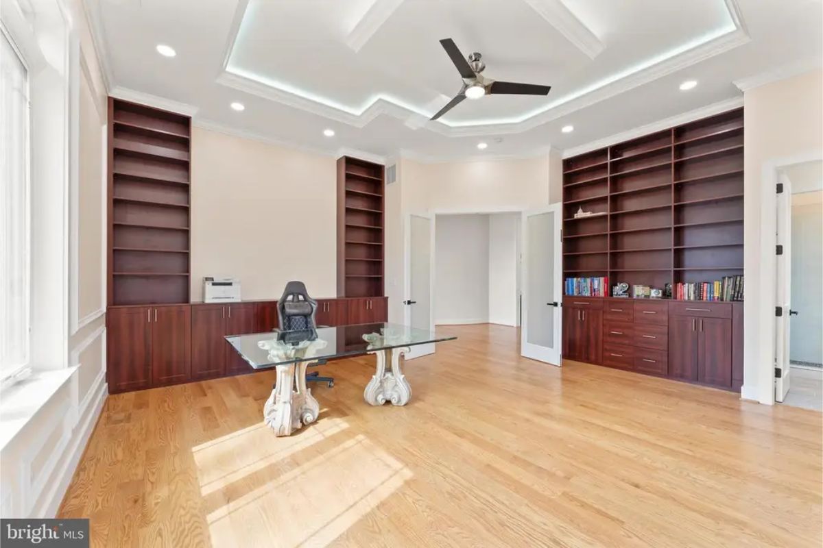 Office with coffered ceiling, built-in shelves, and two glass-top desks. 