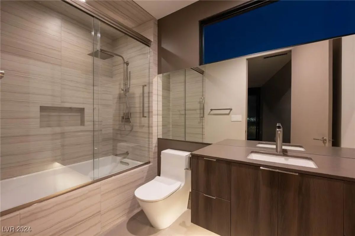 Modern bathroom with wood-accented vanity, double sinks, and a glass-enclosed tub-shower combo.