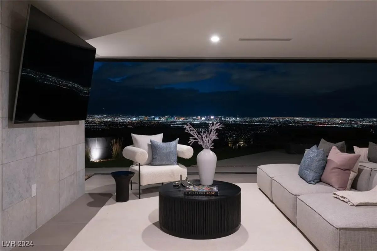 Lounge area with sectional sofa, large-screen TV, and full window wall showcasing city lights at night.