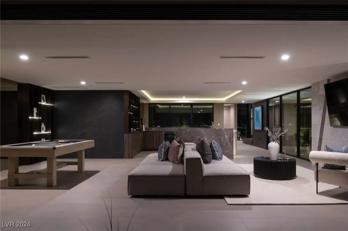 Open-concept entertainment room with sectional seating, pool table, and glass doors leading outside.