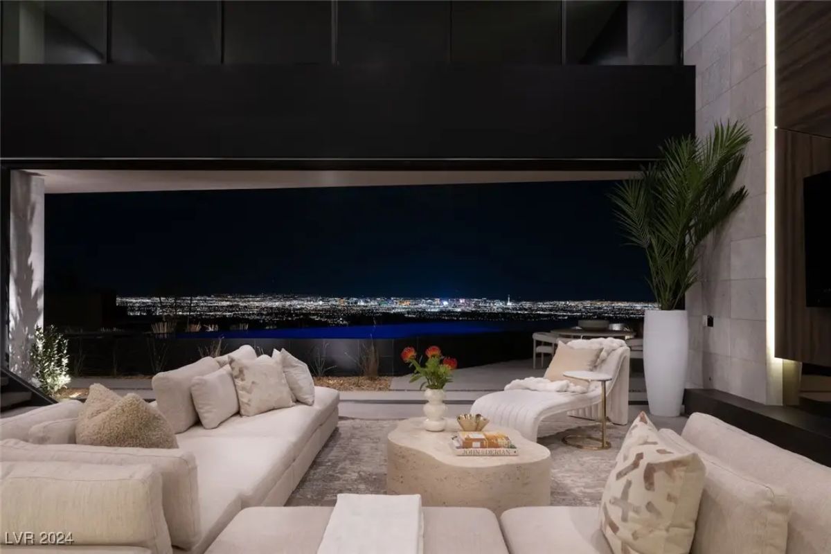 Living room with sectional sofas and panoramic nighttime views through retractable glass wall.