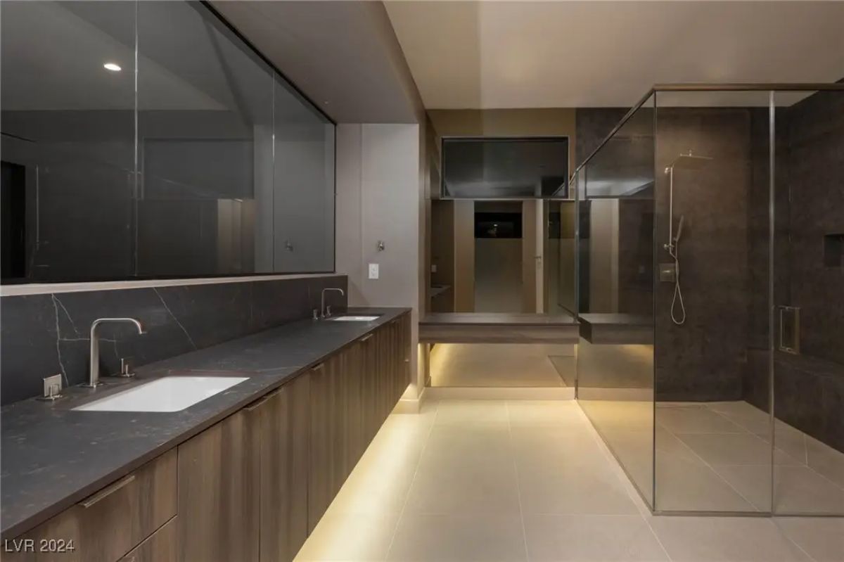 Spacious contemporary bathroom with dark double vanity, underlit floating cabinets, and a large glass shower.