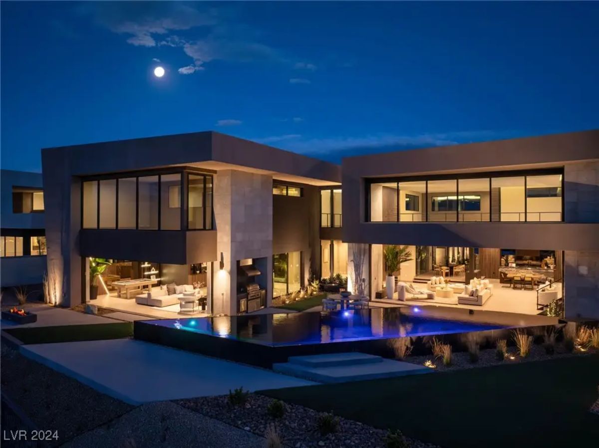 Night view of modern home with floor-to-ceiling windows and illuminated pool.