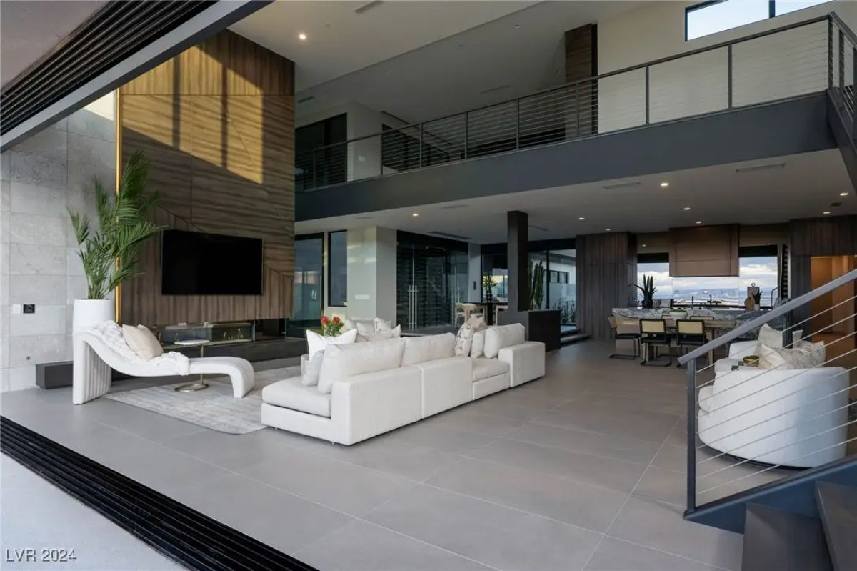 Open-concept living area with balcony above and large sliding doors connecting to outdoor space.