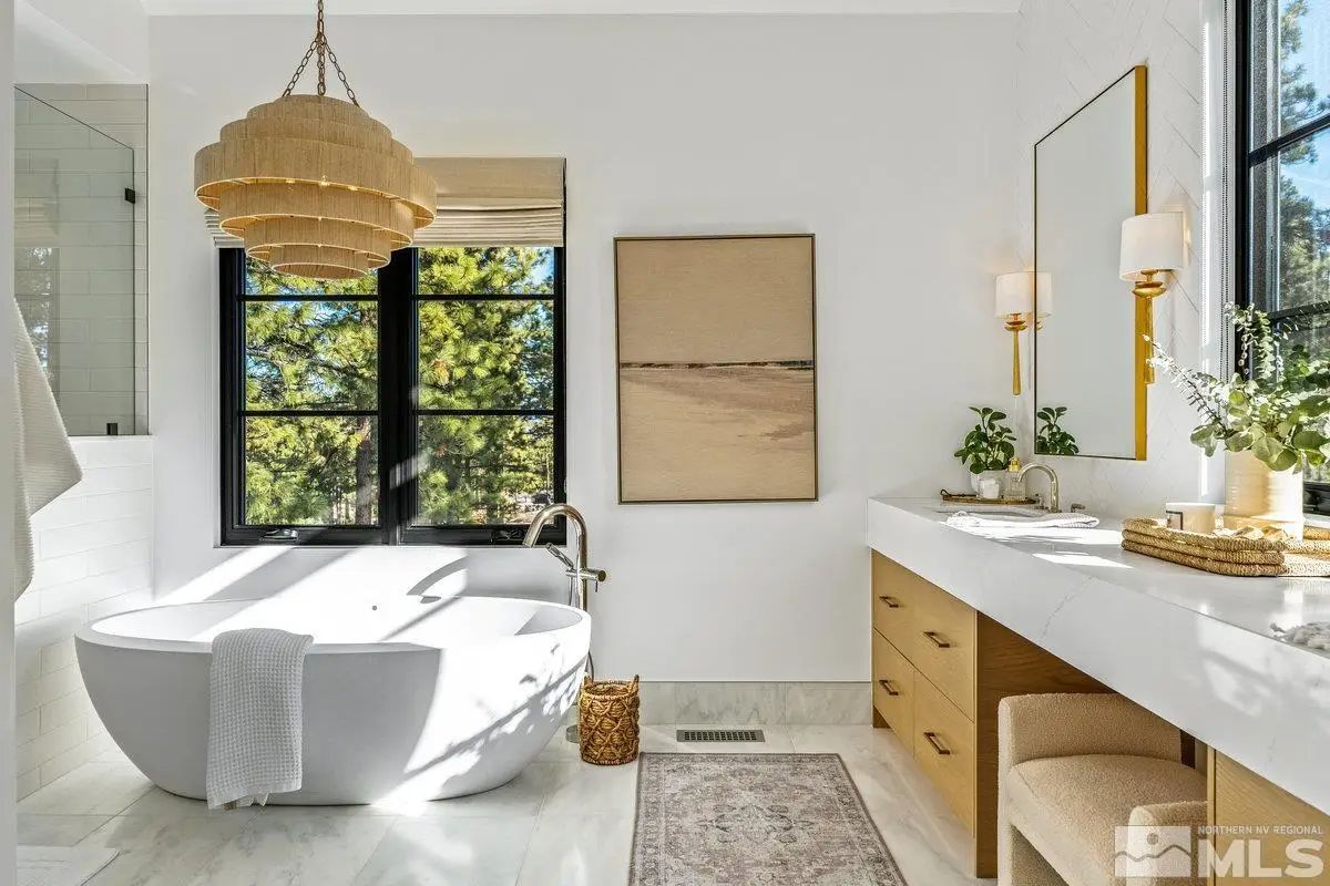 Bathroom with soaking tub, dual vanity, and large window with tree views. 
