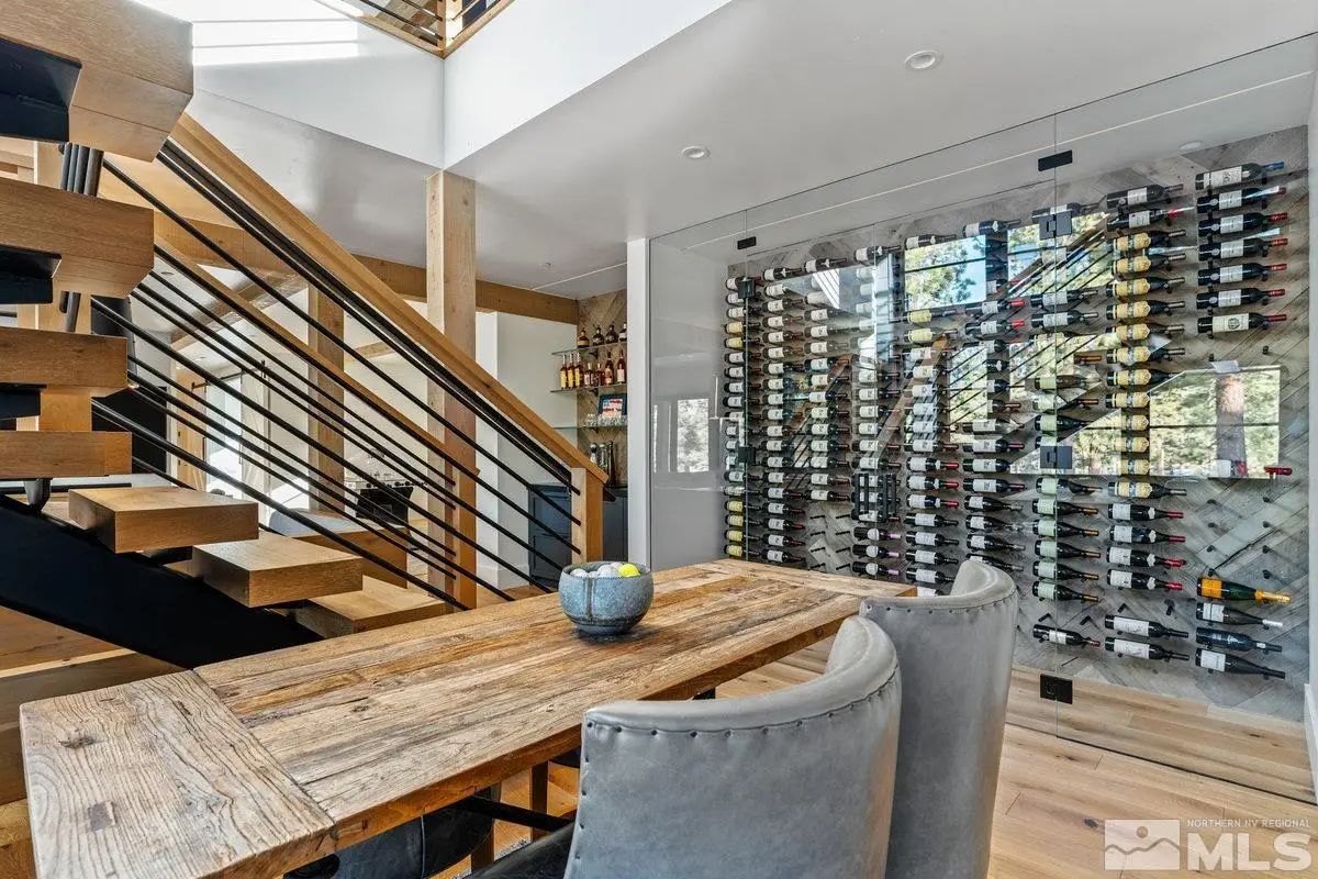 Wine tasting nook with rustic wood table, upholstered chairs, and modern glass wine wall. 