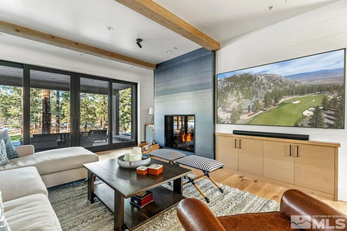 Media room with sectional sofa, built-in fireplace, and wall-mounted TV facing forest views. 