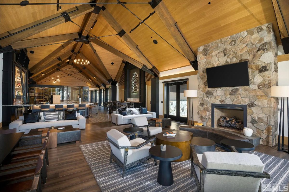 Lodge-style great room with exposed beams, stone fireplace, and multiple seating areas. 