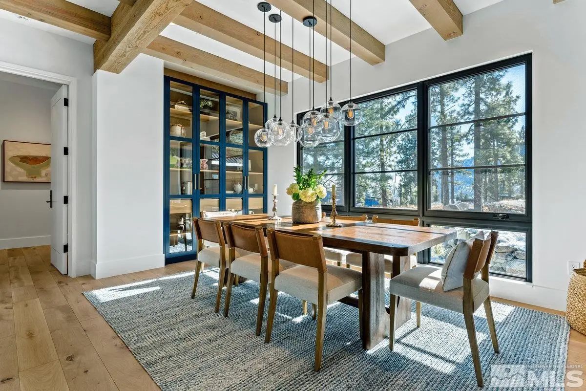 Dining room with wood-beam ceiling, six-seat table, and forest-facing windows. 