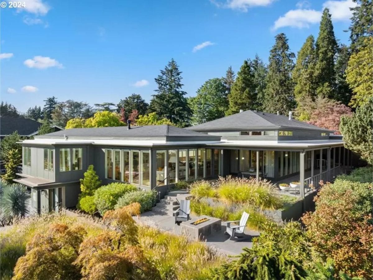 Modern hillside residence surrounded by mature trees and landscaped terraces. 