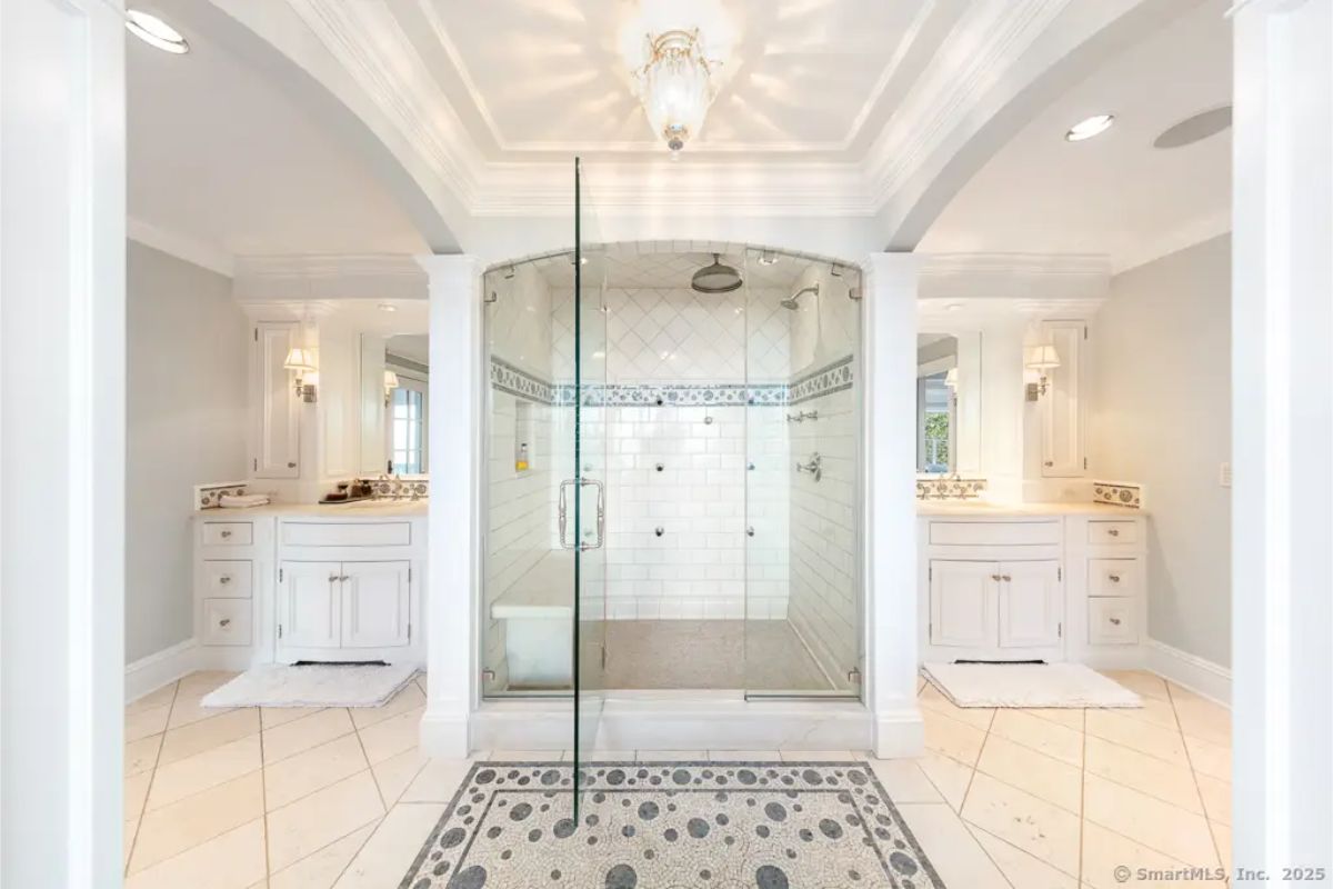 Double vanity bathroom with arched ceiling, central glass-enclosed shower, and symmetrical layout. 