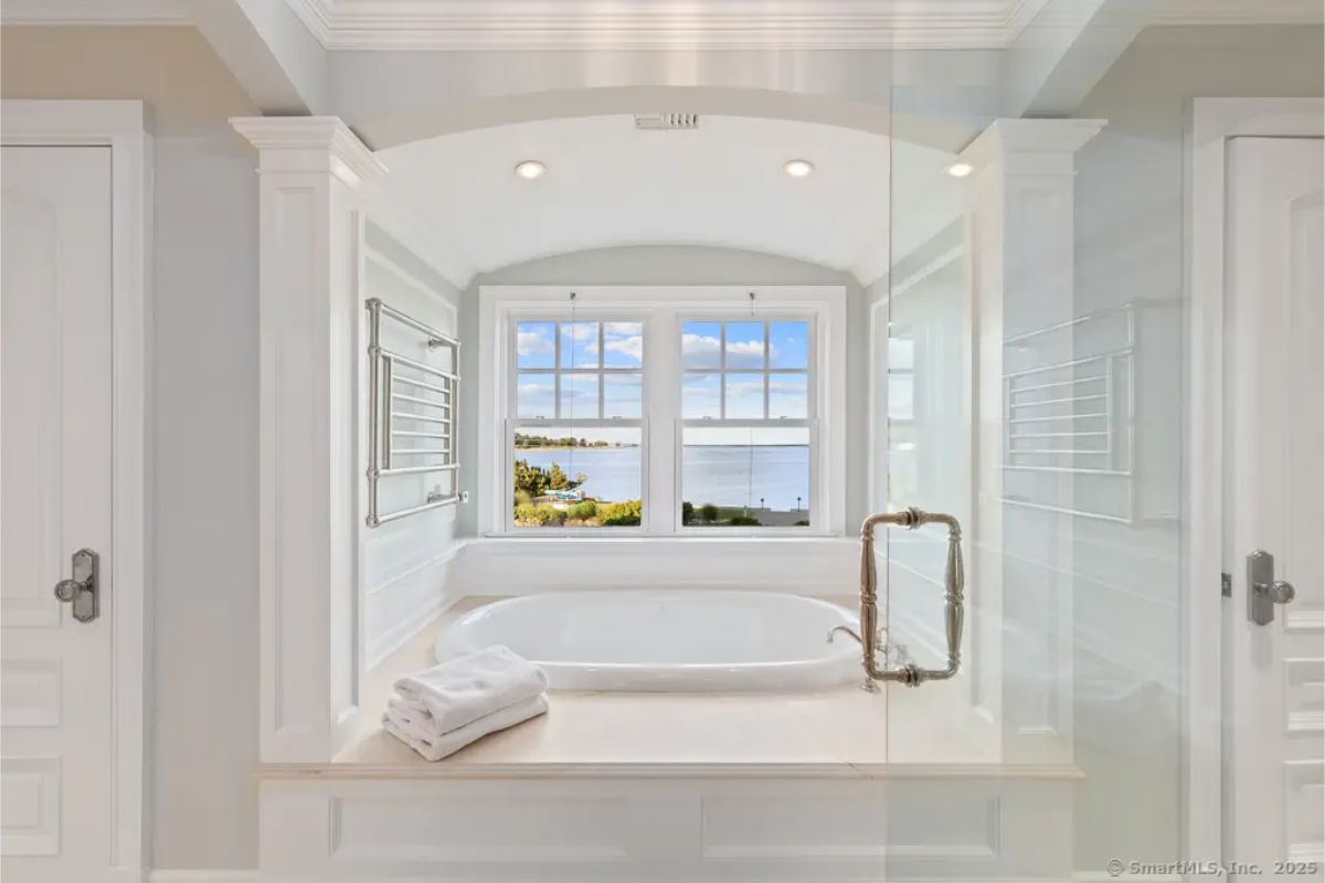 Built-in soaking tub framed by a large picture window with water views and recessed lighting. 