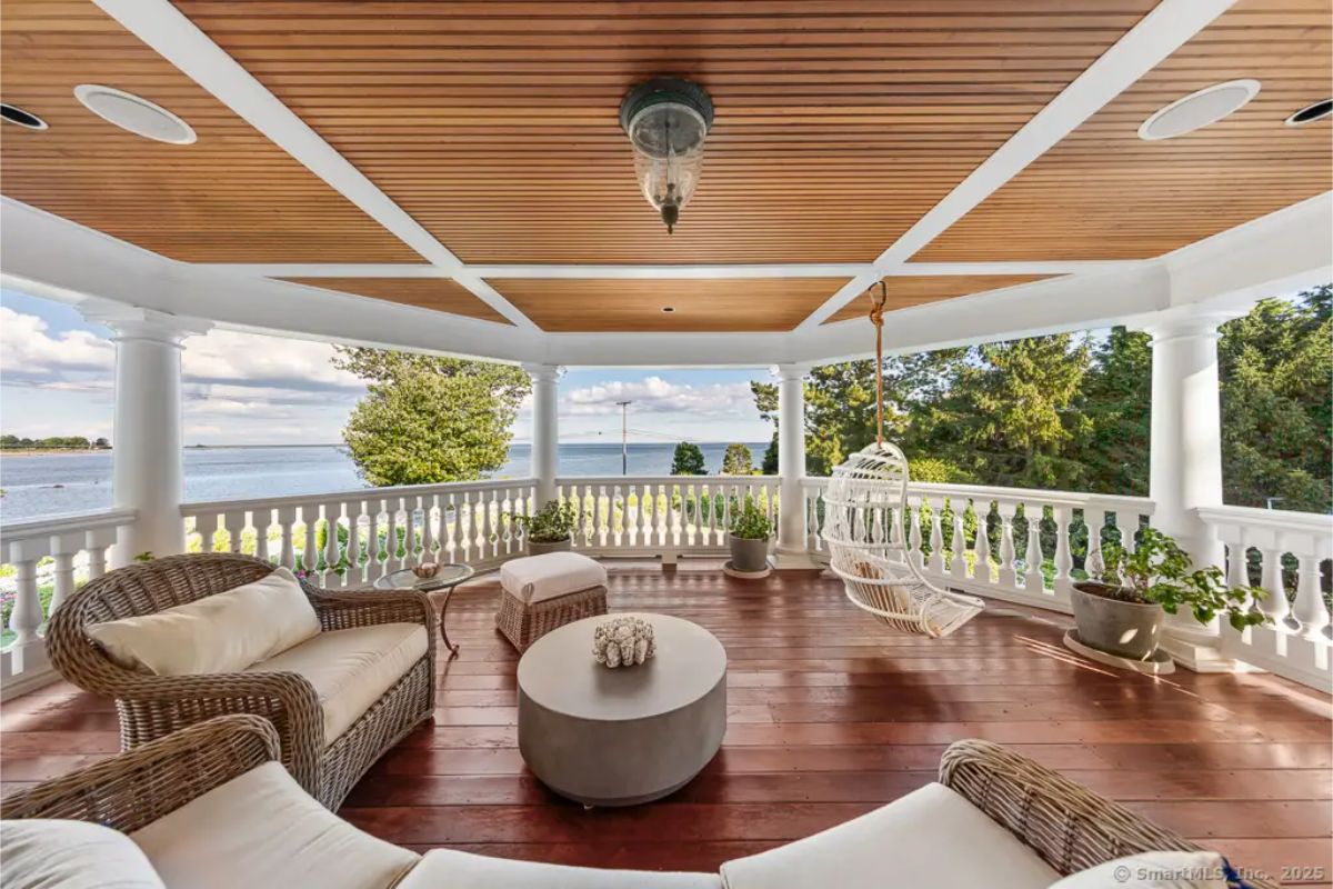 Covered porch with wood ceiling, wicker seating, swing chair, and sweeping views of the water. 