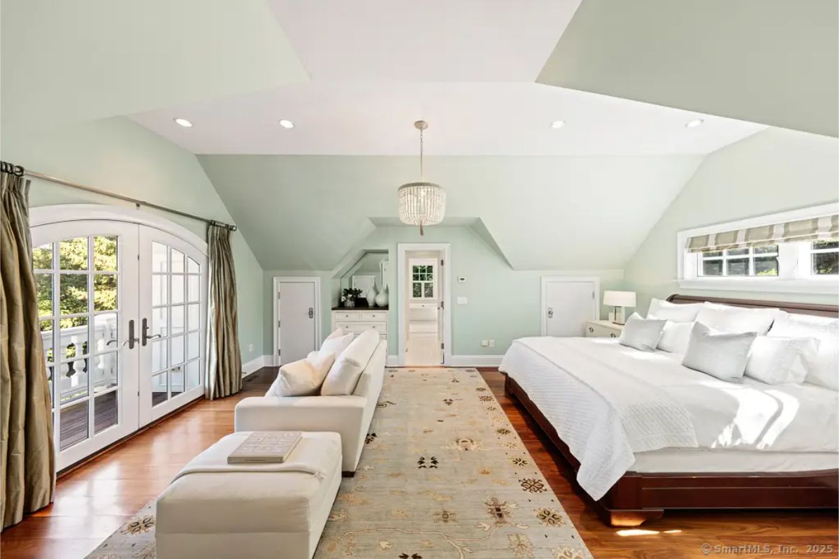 Spacious bedroom with pitched ceiling, seating area, French doors to a balcony, and soft green walls. 