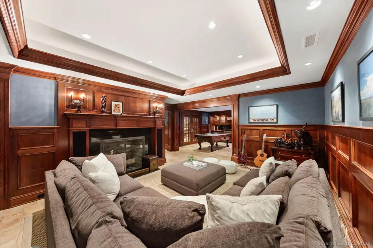 Richly finished entertainment room with fireplace, sectional seating, game area, and wood paneling. 