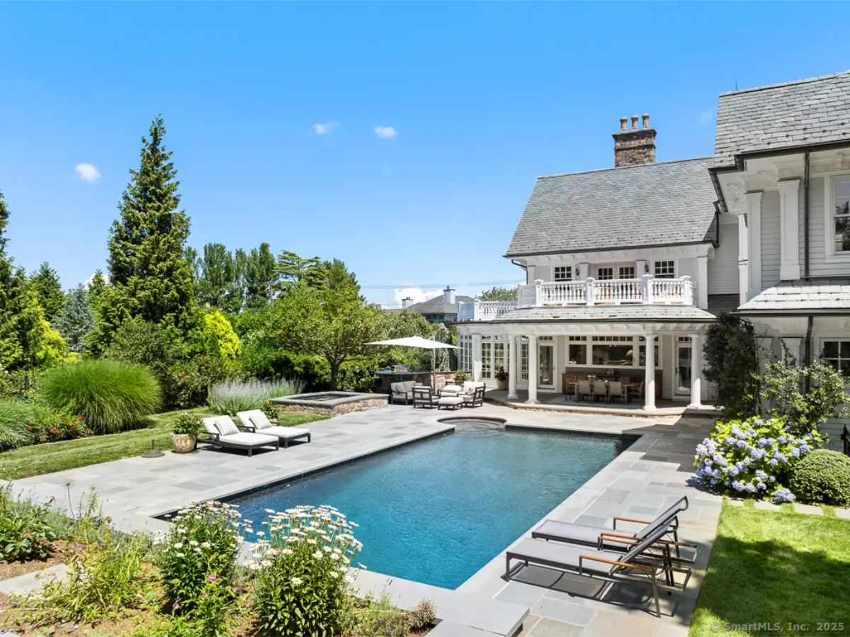 Backyard stone patio with rectangular pool, lounge chairs, lush landscaping, and direct house access. 