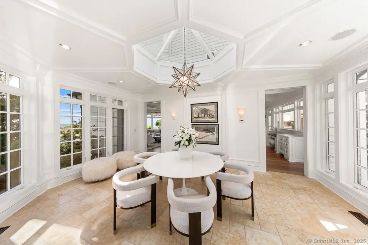 Round breakfast room under a vaulted skylight with white paneling, starburst chandelier, and garden views. 