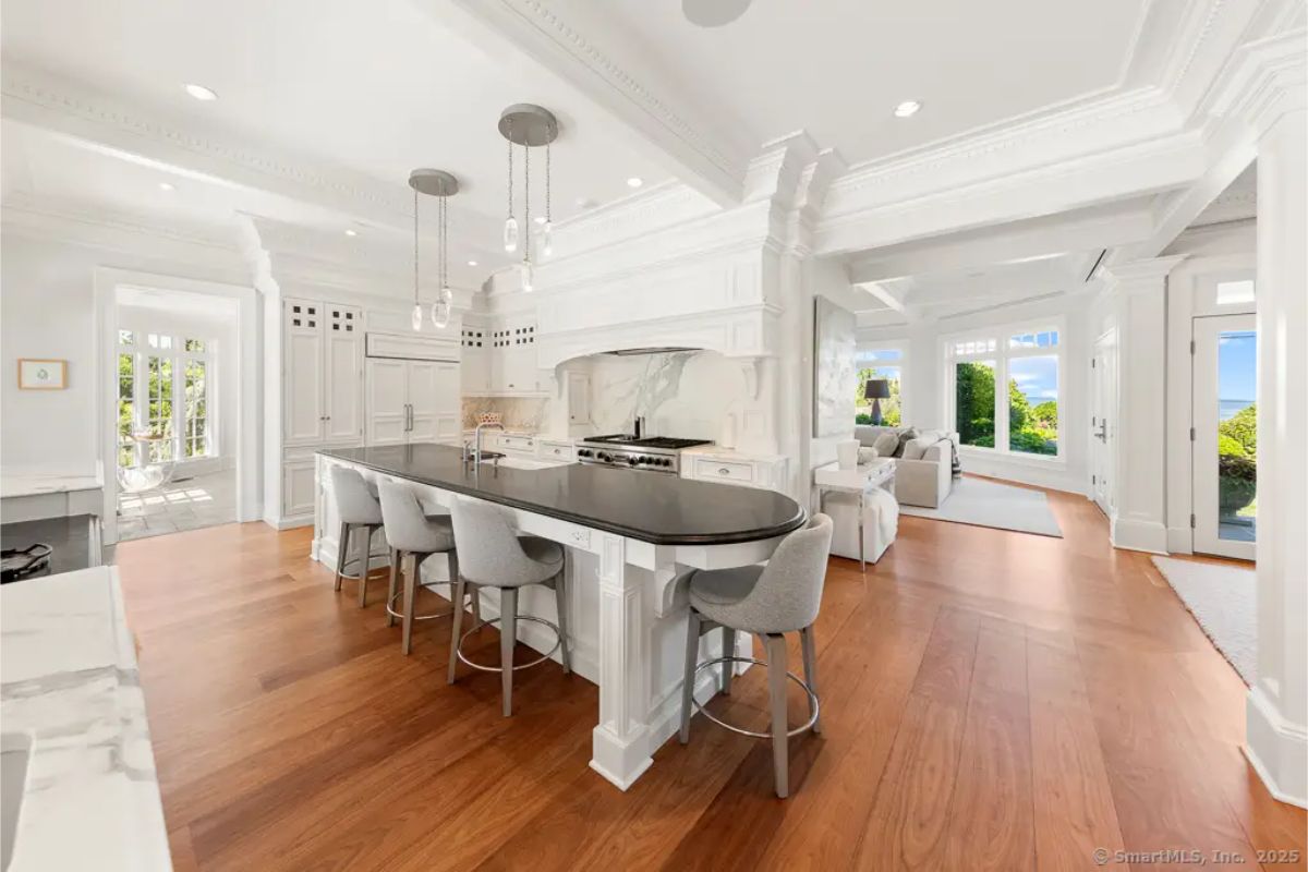 White chef’s kitchen with double islands, marble countertops, pendant lighting, and integrated appliances. 