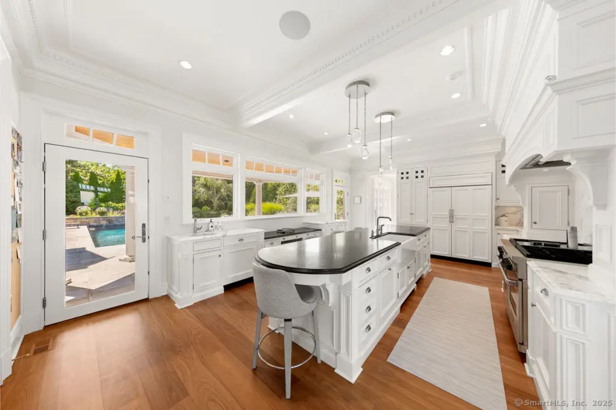 Kitchen view facing the pool terrace, showcasing full-height cabinetry, wide windows, and warm wood flooring. 