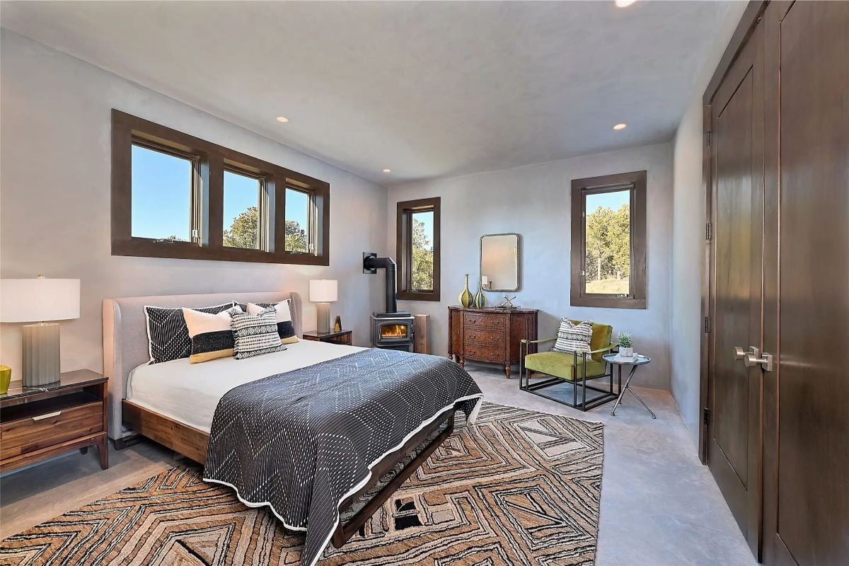 Guest bedroom with large windows, modern decor, and cozy fireplace corner. 