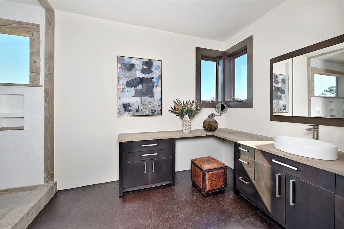 Bathroom with dark cabinetry, round vessel sink, and large corner windows. 