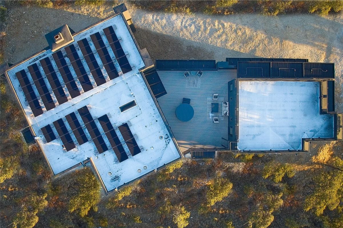 Overhead view of modern home layout with rooftop solar panels and wraparound deck. 