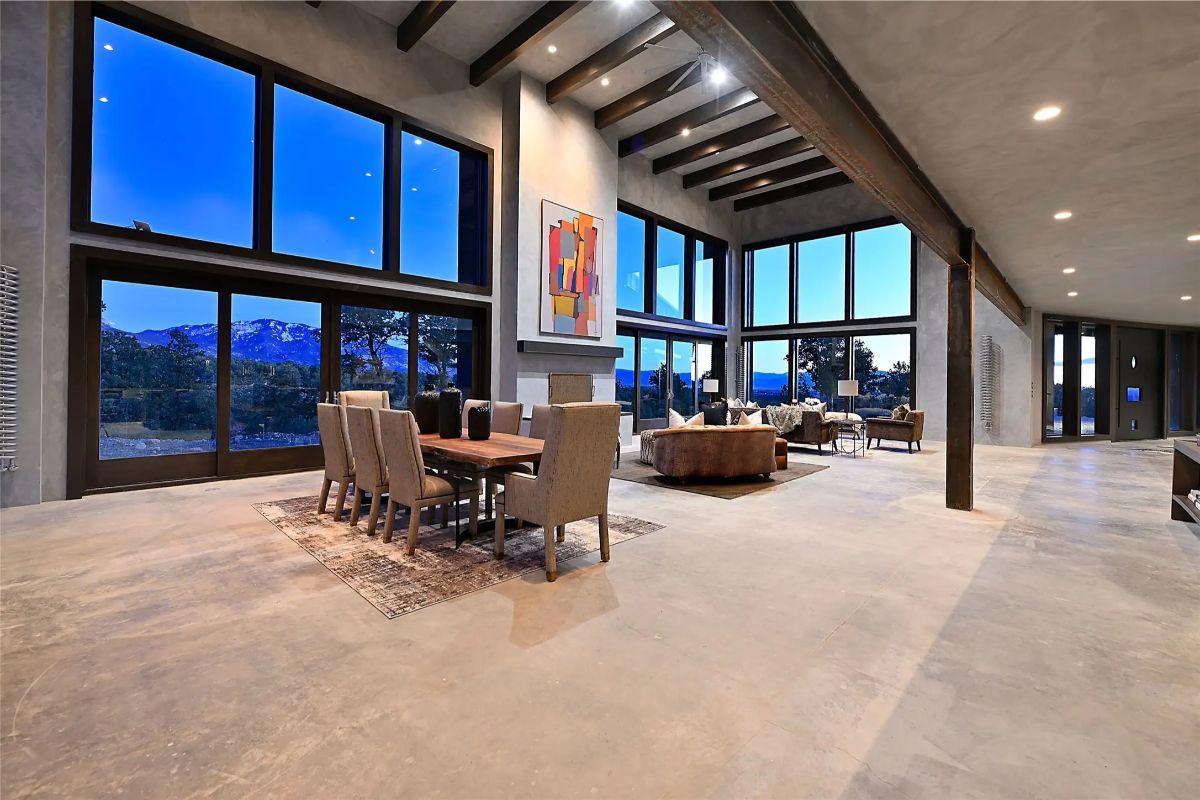Dining area and lounge under vaulted ceiling with full-height windows overlooking trees. 