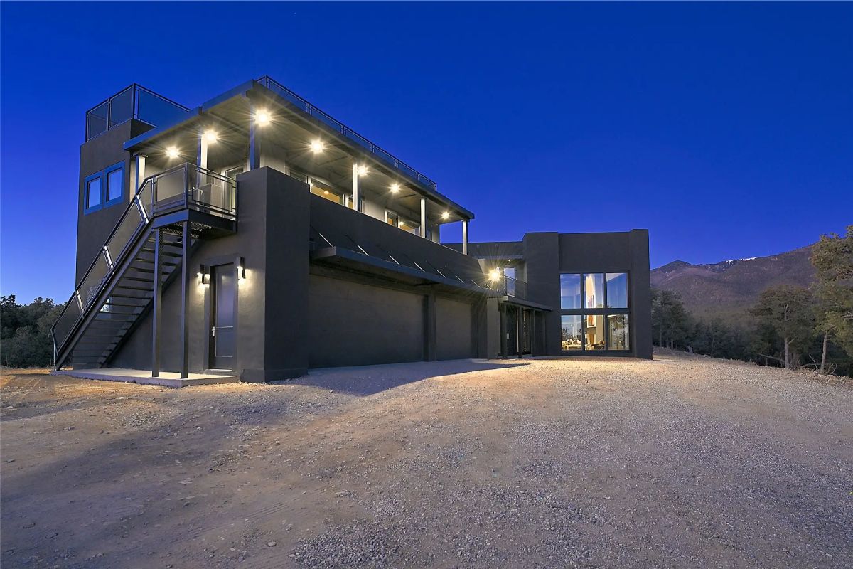 Contemporary exterior with dark facade, upper-level deck, and wide gravel drive. 