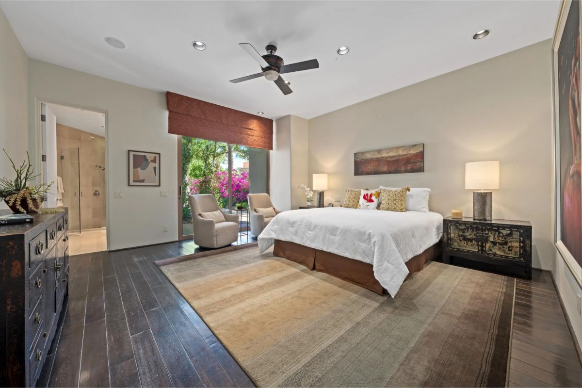 Guest bedroom with dark wood flooring, ceiling fan, and access to a lush patio. 