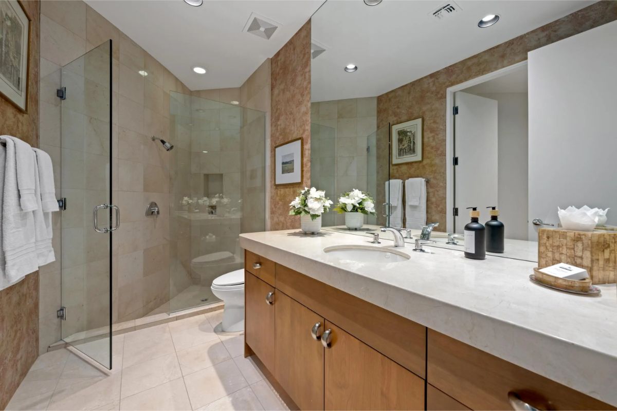 Glass-enclosed walk-in shower and single-sink vanity with light stone countertop. 