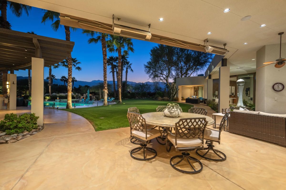 Covered outdoor patio with dining table and lawn views at dusk. 