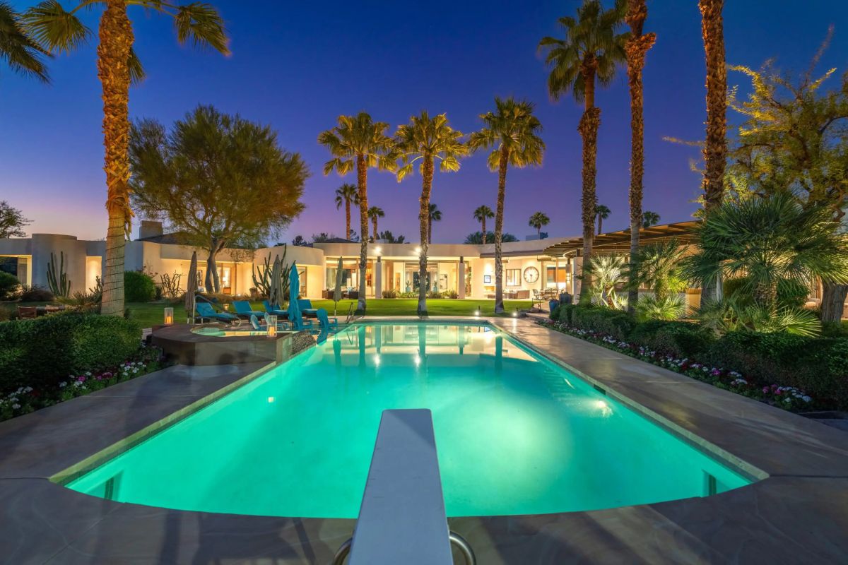 Illuminated rectangular pool surrounded by palm trees and landscaped gardens. 