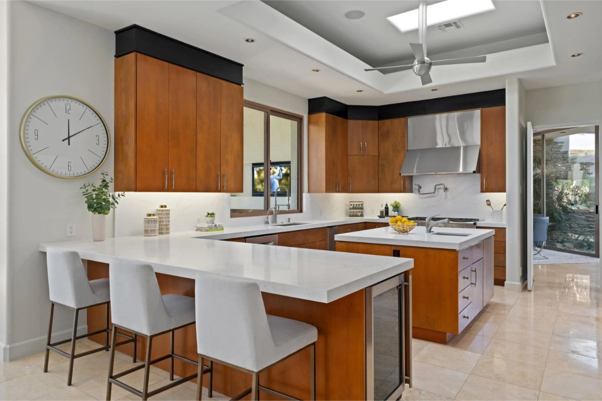 Sleek kitchen with white countertops, warm wood cabinetry, and stainless steel appliances. 