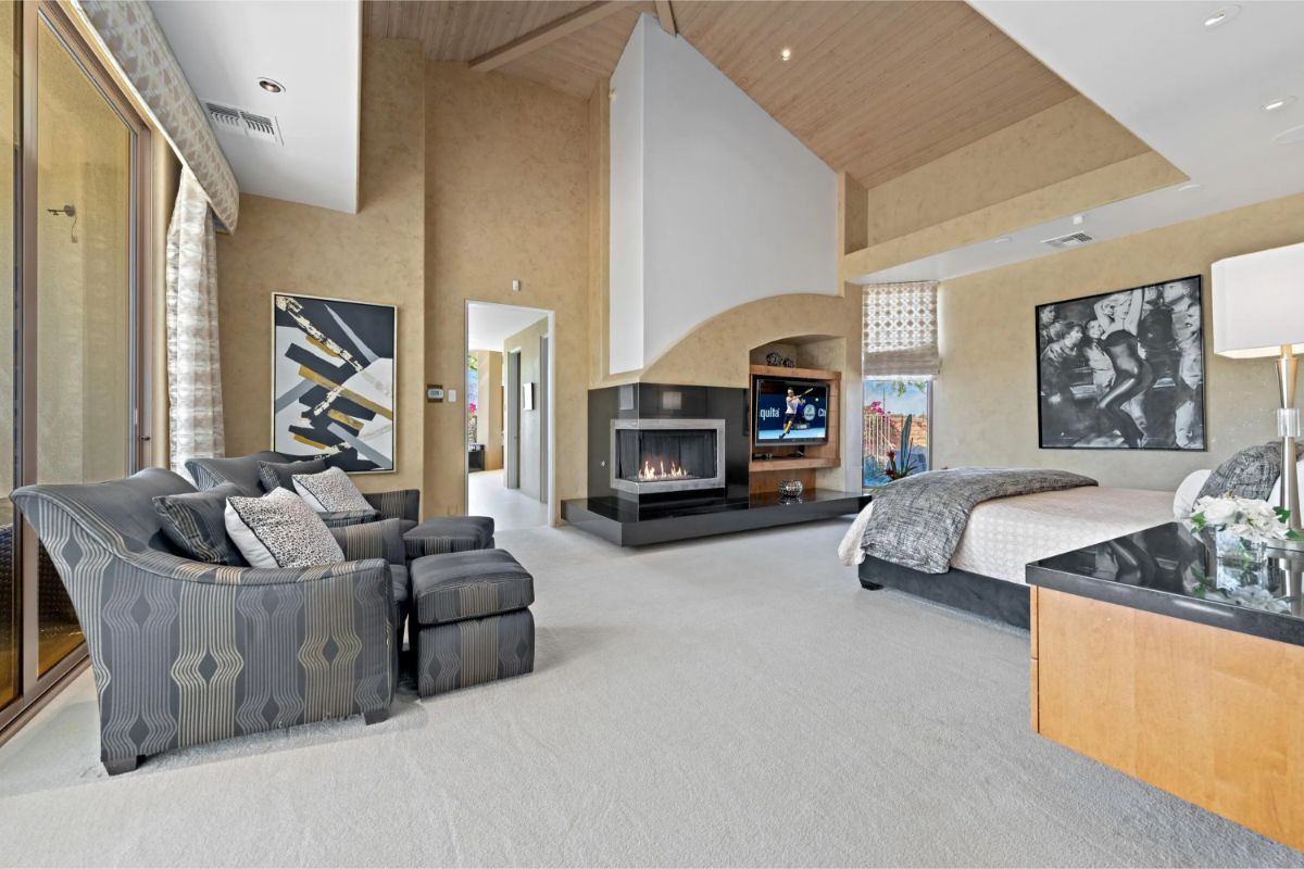 Spacious primary bedroom with fireplace, lounge area, vaulted ceiling, and large TV. 
