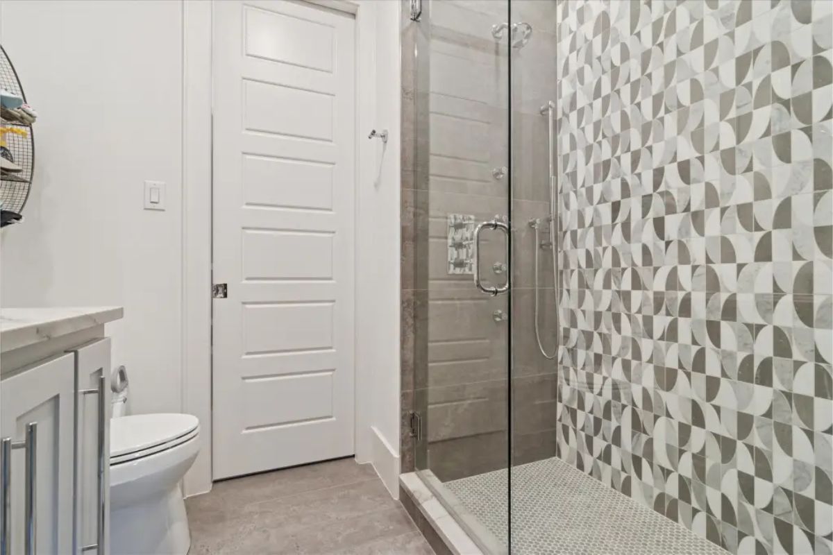 Bathroom with glass-enclosed shower featuring geometric tile accent wall. 