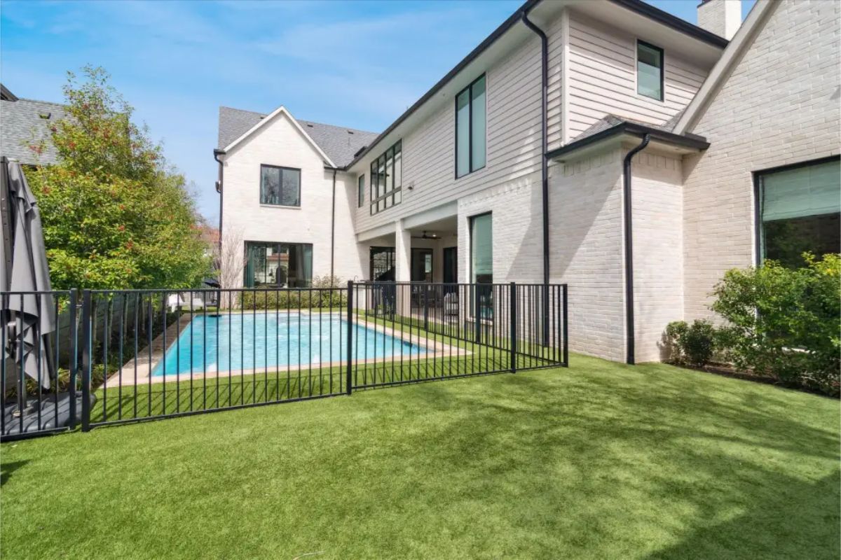 Fenced backyard with pool and artificial turf adjacent to two-story home. 
