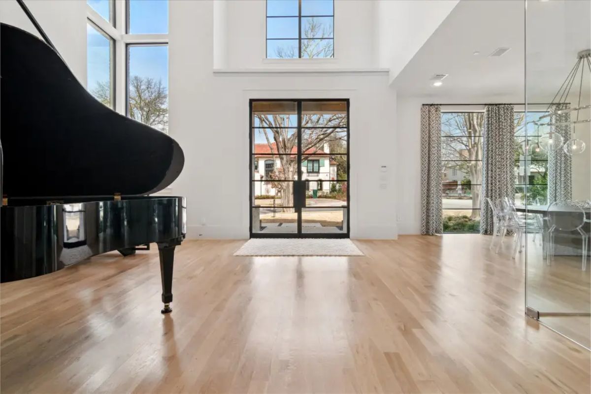 Entry foyer with light wood flooring, double-height ceilings, and a grand piano. 