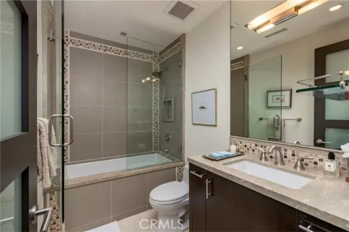 Guest bathroom with glass-enclosed tub, mosaic tile accents, and modern vanity. 