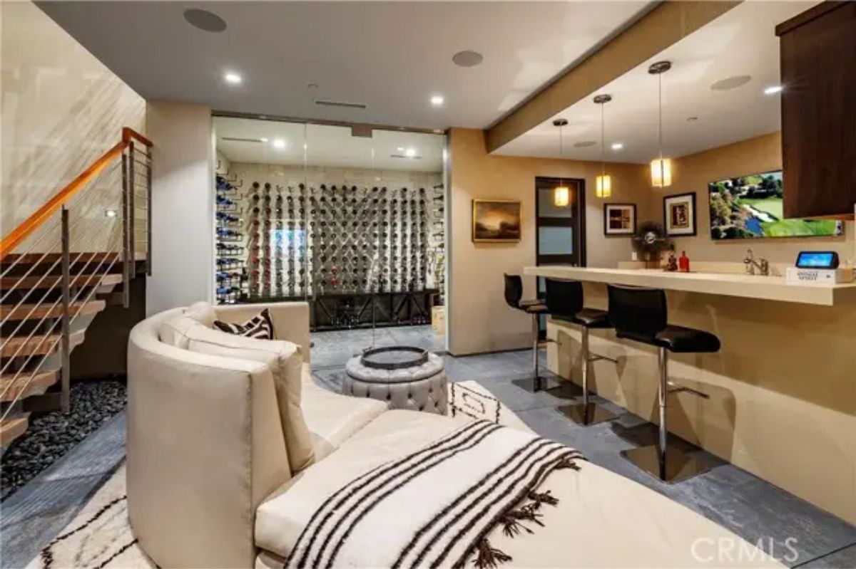 Lounge and bar area with curved seating, counter bar, and glass-enclosed wine cellar. 
