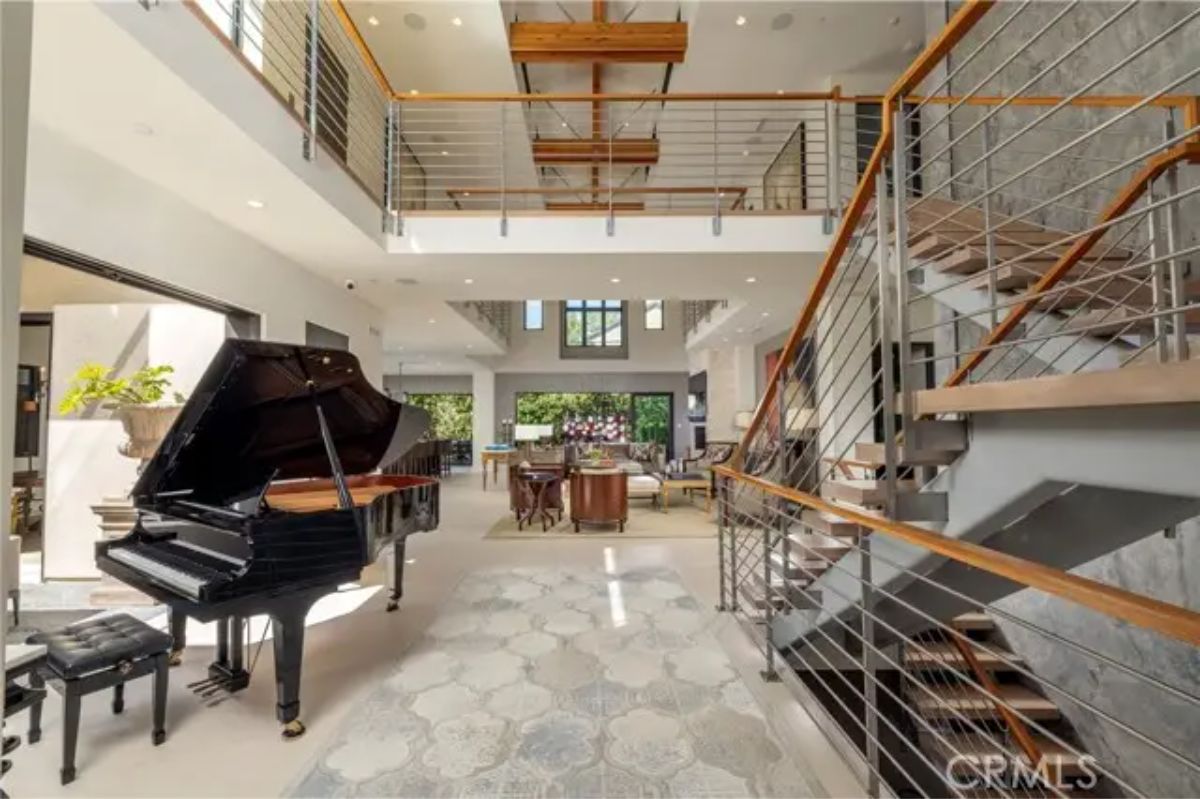 Double-height foyer with grand piano, floating staircase, and open mezzanine level. 